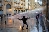 A demonstrator throws a stone as police use water cannon during a protest in Beirut