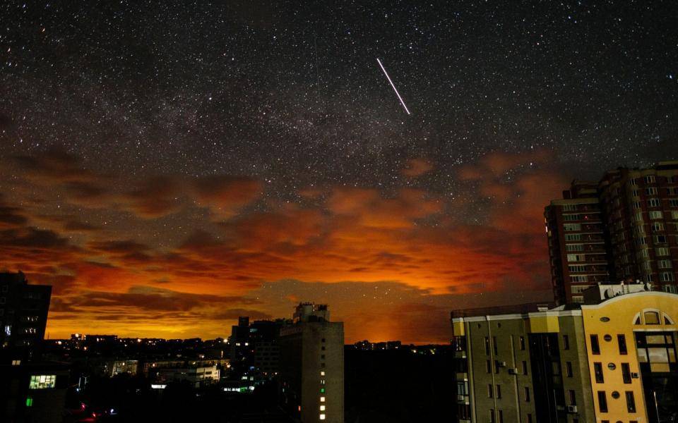 A photo taken using a slow shutter speed shows the orange glow of an ongoing battle projected on the clouds as a satellite crosses the starry sky above the outskirts of Kharkiv, Ukraine - PAVLO PAKHOMENKO/Shutterstock