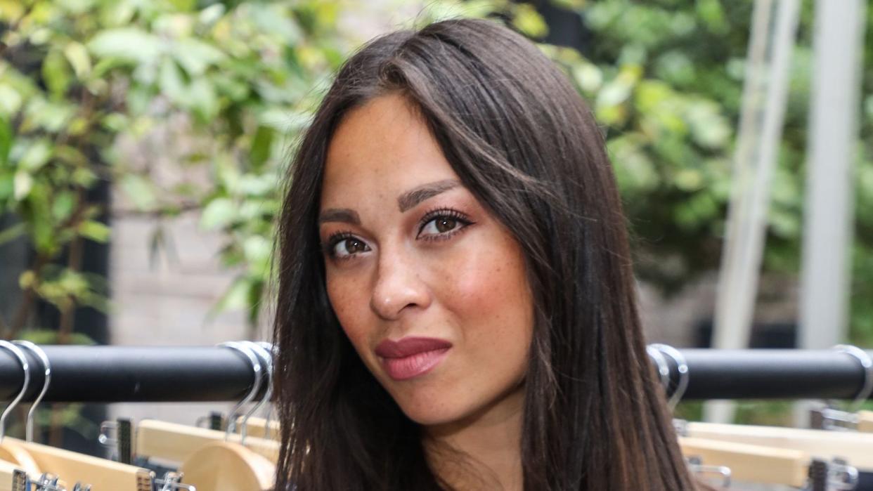 Katya Jones in blue dress in front of clothes rack of jeans