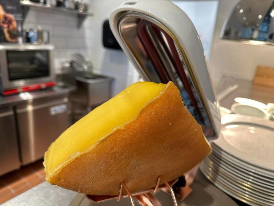 A wheel of raclette cheese from Switzerland is broiled until it starts to melt. The melted cheese will then be sliced over torn warm bread.