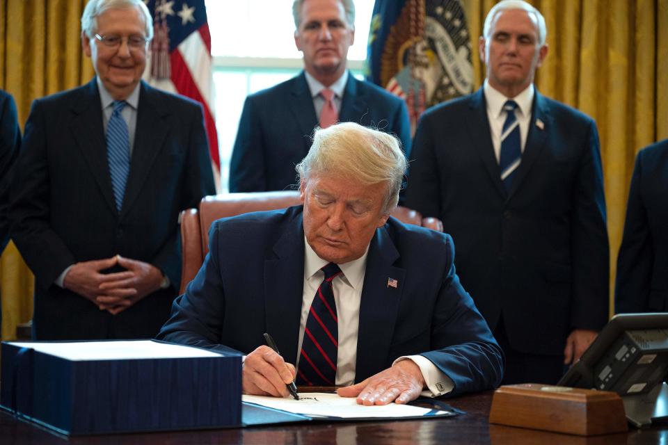 US President Donald Trump signs the CARES act, a $2 trillion rescue package to provide economic relief amid the coronavirus outbreak, at the Oval Office of the White House on March 27, 2020. - After clearing the Senate earlier this week, and as the United States became the new global epicenter of the pandemic with 92,000 confirmed cases of infection, Republicans and Democrats united to greenlight the nation's largest-ever economic relief plan. (Photo by JIM WATSON / AFP) (Photo by JIM WATSON/AFP via Getty Images)