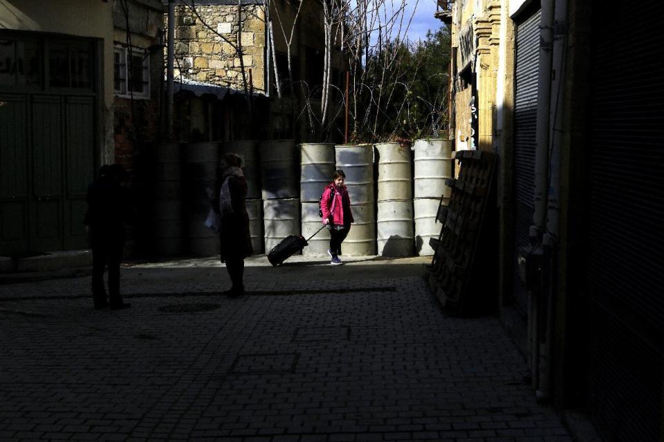 A young woman pulls her travel case as she walks by the barrels that blocked a road from the Greek Cypriot controlled area, to the Turkish Cypriot north, wld in the divided capital Nicosia in the eastern Mediterranean island of Cyprus, on Thursday, Feb. 16, 2017. The leader of ethnically divided Cyprus' breakaway Turkish Cypriots has walked out of a meeting with the Greek Cypriot president amid ongoing reunification talks. It's unclear why Mustafa Akinci left Thursday's meeting with Nicos Anastasiades and what this means to the months-long peace process. (AP Photo/Petros Karadjias)