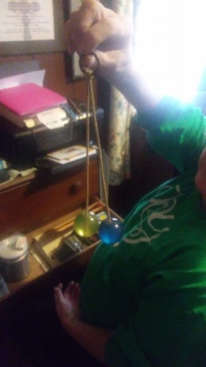 Person holding a pair of Newton's cradle balls, one green and one blue, by strings in a home office setting