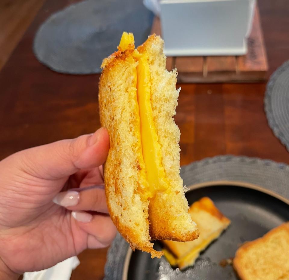 Person holding a half-eaten grilled cheese sandwich, with melted cheese visible