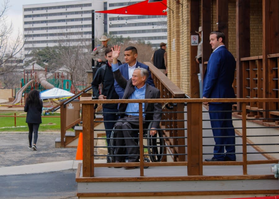 Gov. Greg Abbott pauses to wave at the group of protestors before making his way inside the Central Firehouse Pizzeria