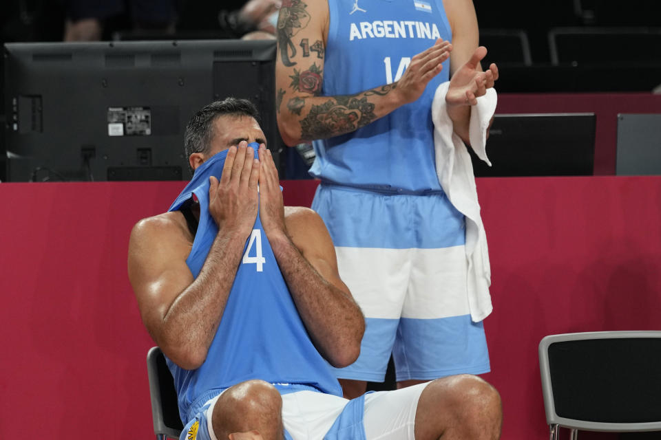 Argentina's Luis Scola (4) pulls his jersey over his face as he receives an emotional standing ovation from his team, Australia players, and others in attendance when he was pulled from the game in the final moments of a men's basketball quarterfinal round game at the 2020 Summer Olympics, Tuesday, Aug. 3, 2021, in Saitama, Japan. (AP Photo/Eric Gay)