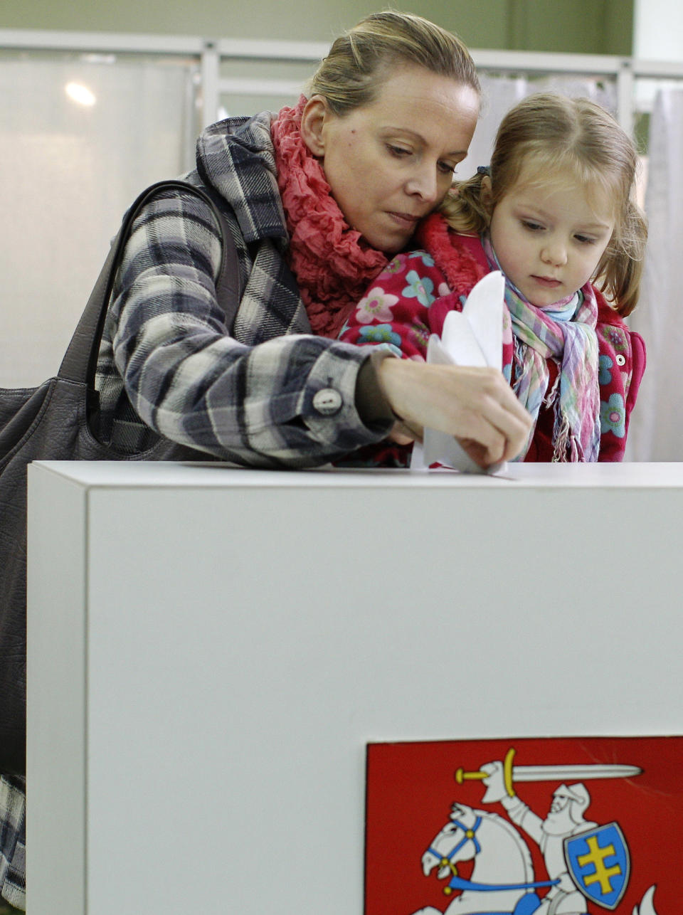 A woman with a child casts her ballot at a polling station in Vilnius, Lithuania, Sunday, Oct. 14, 2012. Lithuanians are expected to deal a double-blow to the incumbent conservative government in national elections Sunday by handing a victory to opposition leftists and populists and saying 'no' to a new nuclear power plant that supporters claim would boost the country's energy independence. (AP Photo/Mindaugas Kulbis)