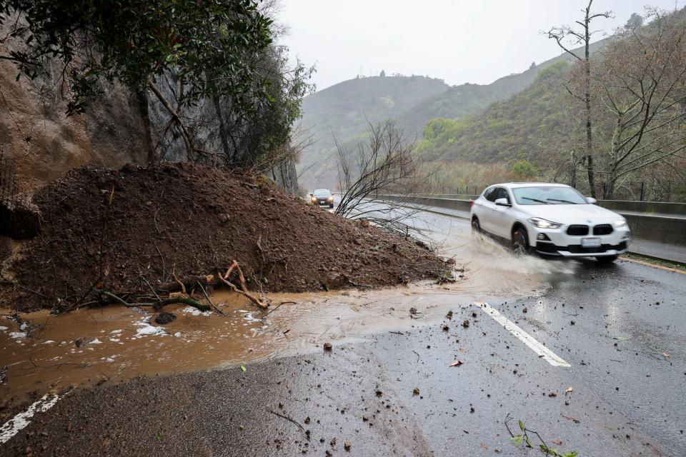 car drives around landslide pile of dirt ringed with floodwater blocking mountain highway
