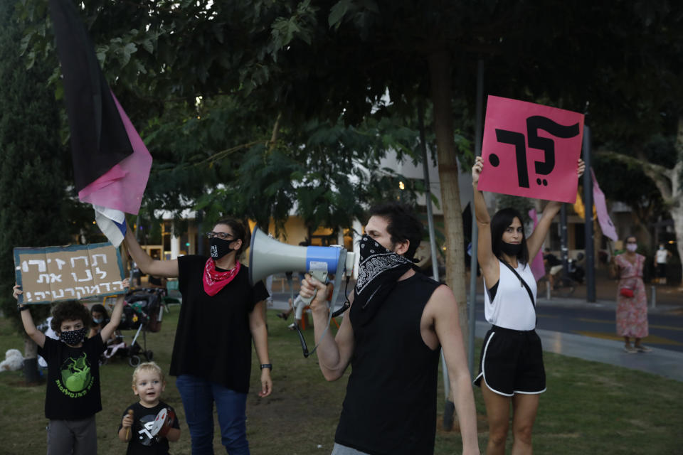 A woman holds a placard that reads, "go," right, and a child holds another reading, "bring our democracy back," during a protest against Prime Minister Benjamin Netanyahu in Tel Aviv, Israel, Thursday, Oct. 8, 2020 during a nationwide lockdown to curb the spread of the coronavirus. The Israeli government has extended an emergency provision that bars public gatherings, including widespread protests against Netanyahu, for an additional week. (AP Photo/Ariel Schalit)