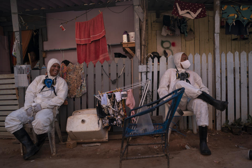 Welington Goncalves, right, sits next to his colleague as they wait to refill their tanks during a disinfection to help contain the spread of the new coronavirus in an area occupied by squatters in a poor region of Rio de Janeiro, Brazil, Friday, June 26, 2020. For the 21-year-old volunteer, who lives in this occupation, the sanitization is a way to avoid the COVID-19 and if it was not for him and other volunteers working on it, "the situation would be worse". (AP Photo/Leo Correa)