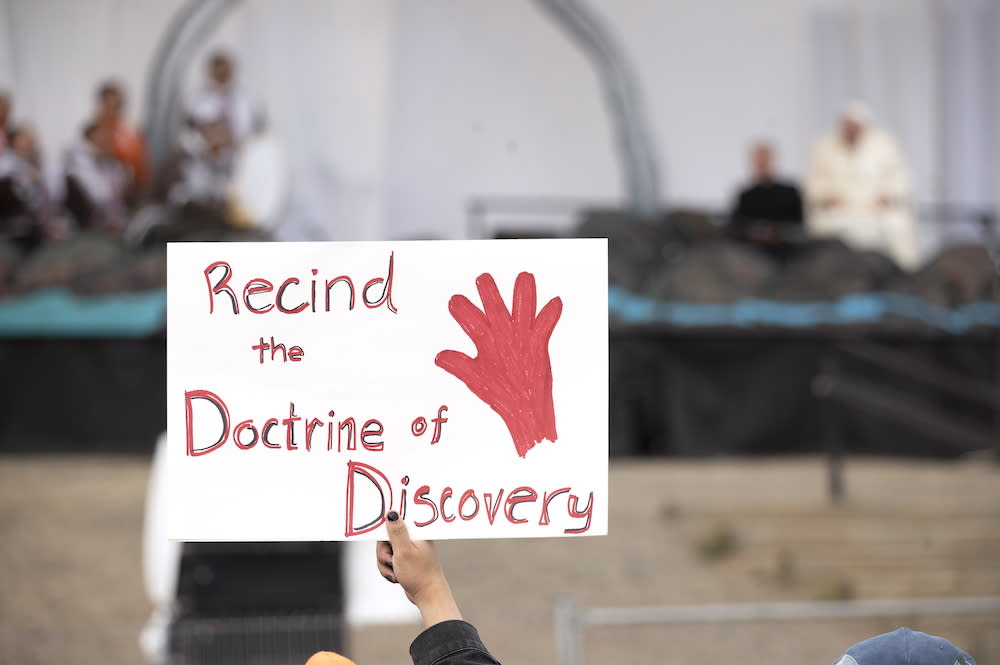 A protester holds a sign as Pope Francis takes part in a public event in Iqaluit, Nunavut, Friday, July 29, 2022, during his papal visit across Canada. (Dustin Patar/The Canadian Press via AP)