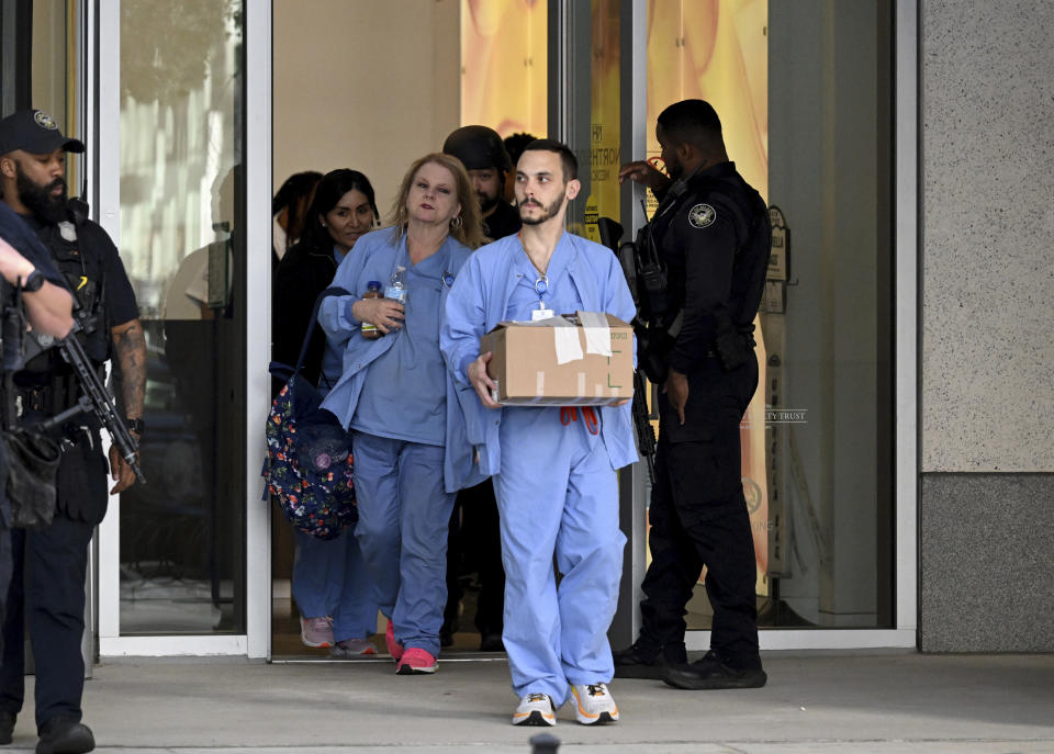 FILE - Law enforcement personnel wath as healthcare workers leave the Northside Hospital Midtown medical office building, Wednesday, May 3, 2023, in Atlanta, where a man opened fire in the medical center waiting room, killing one woman and wounding four. Data shows American health care workers now suffer more nonfatal injuries from workplace violence than workers in any other profession, including law enforcement. (Hyosub Shin/Atlanta Journal-Constitution via AP)