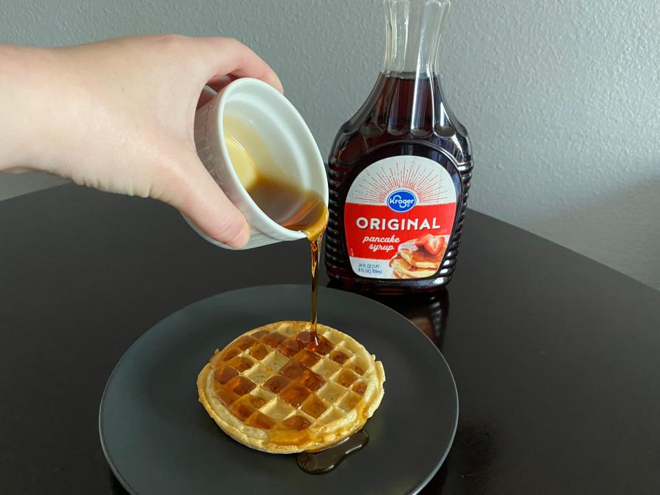 hand pouring white ramekin filled with kroger syrup over a frozen waffle