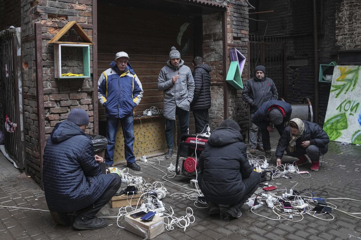 People stand and crouch as they charge their phones in a courtyard in Mariupol. 