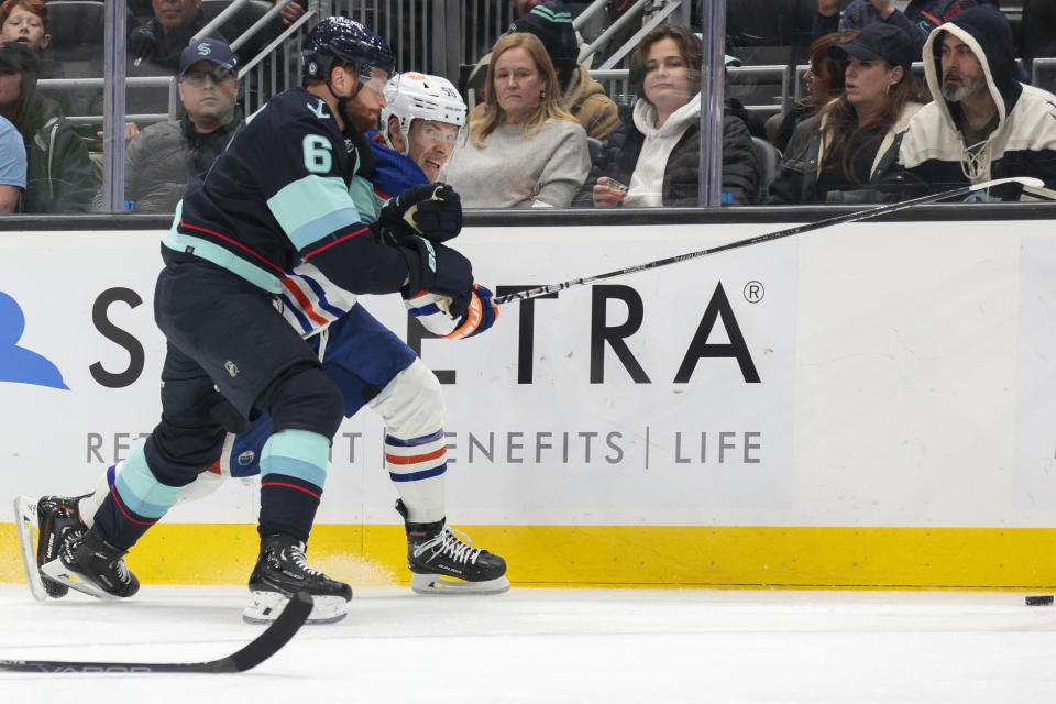 Edmonton Oilers left wing Dylan Holloway, right, and Seattle Kraken defenseman Adam Larsson (6) chase the puck during the second period of an NHL hockey game Saturday, Nov. 11, 2023, in Seattle. (AP Photo/Jason Redmond)