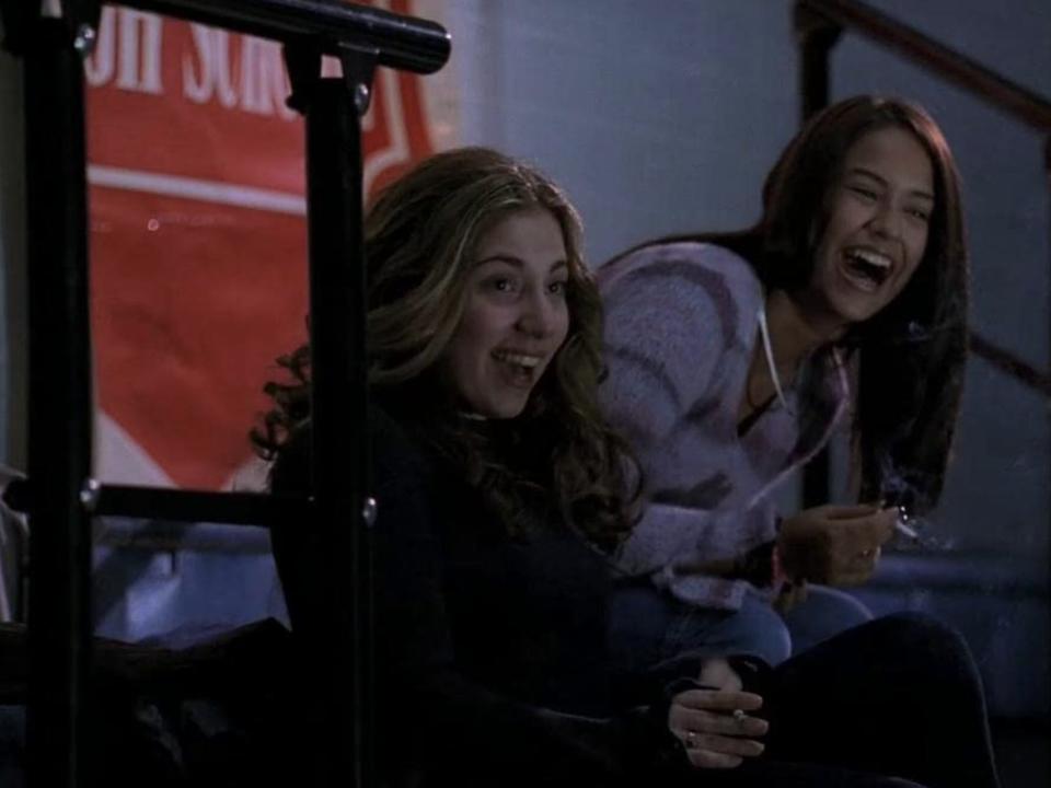 A young Gaga in with brown hair sitting and laughing on bleachers next to another girl.