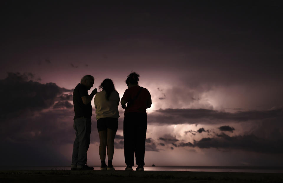 Armando Perez, left, and Gabby Perez, right flank their niece, Victoria Perez, as they watch lightning illuminating the sky at Montrose Harbor as a storm moves over the Lake Michigan following two days unseasonably warm weather, Tuesday, Feb. 27, 2024. (Chris Sweda/Chicago Tribune via AP)