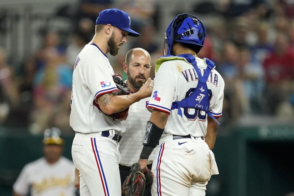 Texas Rangers relief pitcher Joe Barlow, left, and catcher Meibrys Viloria visit with athletic trainer Jacob Newburn, center in the sixth inning of a baseball game against the Oakland Athletics, Wednesday, Aug. 17, 2022, in Arlington, Texas. (AP Photo/Tony Gutierrez)