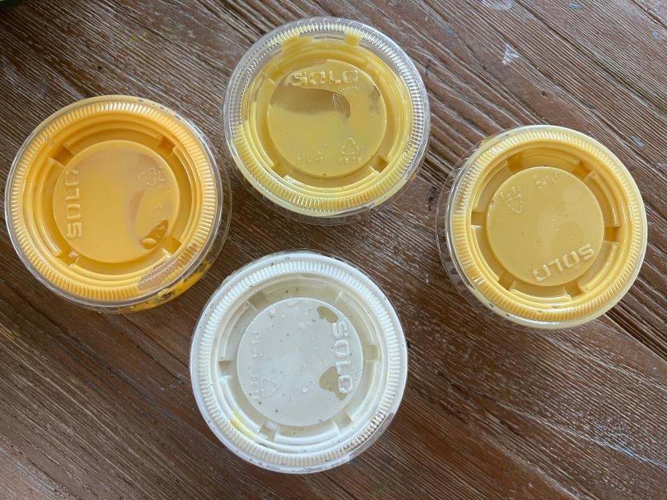 Four containers of sauce. Two are light yellow, one is a dark yellow, and one is white.