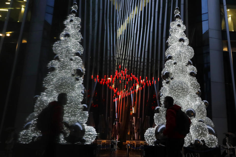 A man is reflected in a window as he walks past a Christmas tree in London, Thursday, Dec. 3, 2020. The European Union on Thursday hit back at a British minister's claim that U.K. vaccine regulators were better than other countries, stressing "this is not a football competition." This came after Britain became the first country in the world to authorize Pfizer's rigorously tested COVID-19 vaccine Wednesday. (AP Photo/Kirsty Wigglesworth)