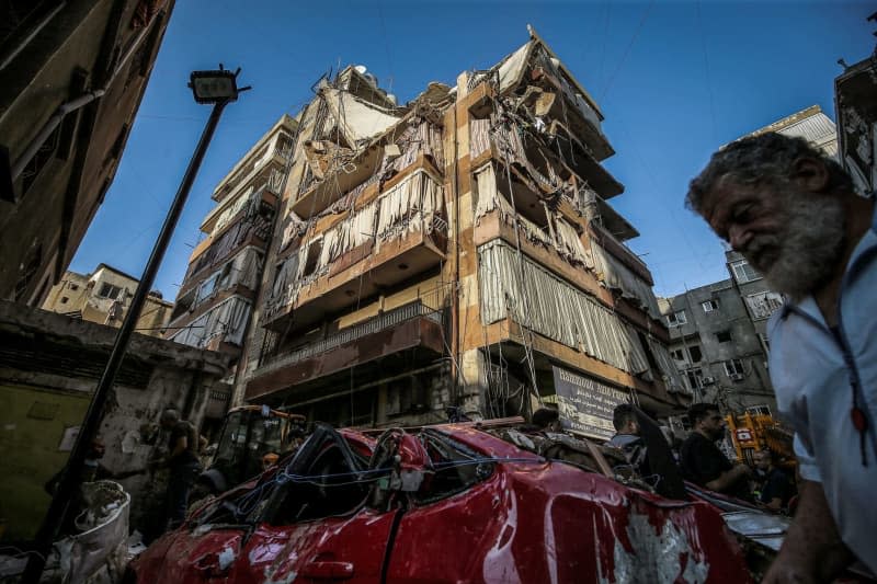 A man passes by a destroyed car and damaged building that were hit by an Israeli airstrike in Beirut southern suburb. According to the Lebanese Ministry of Health, six people were killed and 15 others were wounded in the strike, which was targeting Hezbollah's rocket chief, according to the Israeli military. Marwan Naamani/dpa