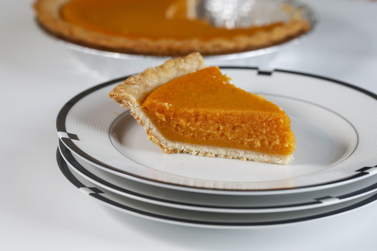 A piece of Patti LaBelle's sweet potato pie on a white porcelain plate on a stack of plates with a blurred background of the rest of the pie