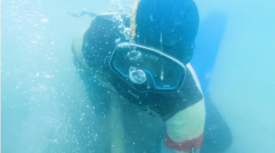 Joko blows bubbles from his scuba mask while holding the vacuum tube in place.