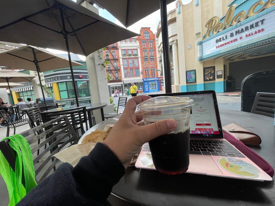 The writer with her laptop sitting outside in Universal holding a coffee