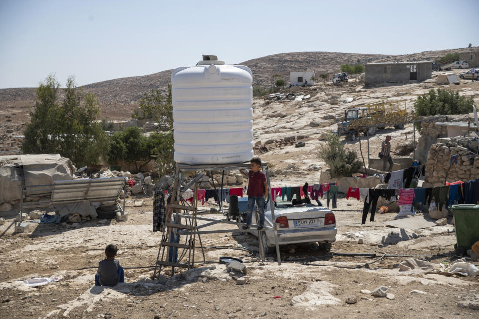 Children play by a new water tank that replaced a damaged one following a settlers' attack from nearby settlement outposts on the Palestinian Bedouin community, in the West Bank village of al-Mufagara, near Hebron, Thursday, Sept. 30, 2021. An Israeli settler attack last week damaged much of the village’s fragile infrastructure. (AP Photo/Nasser Nasser)