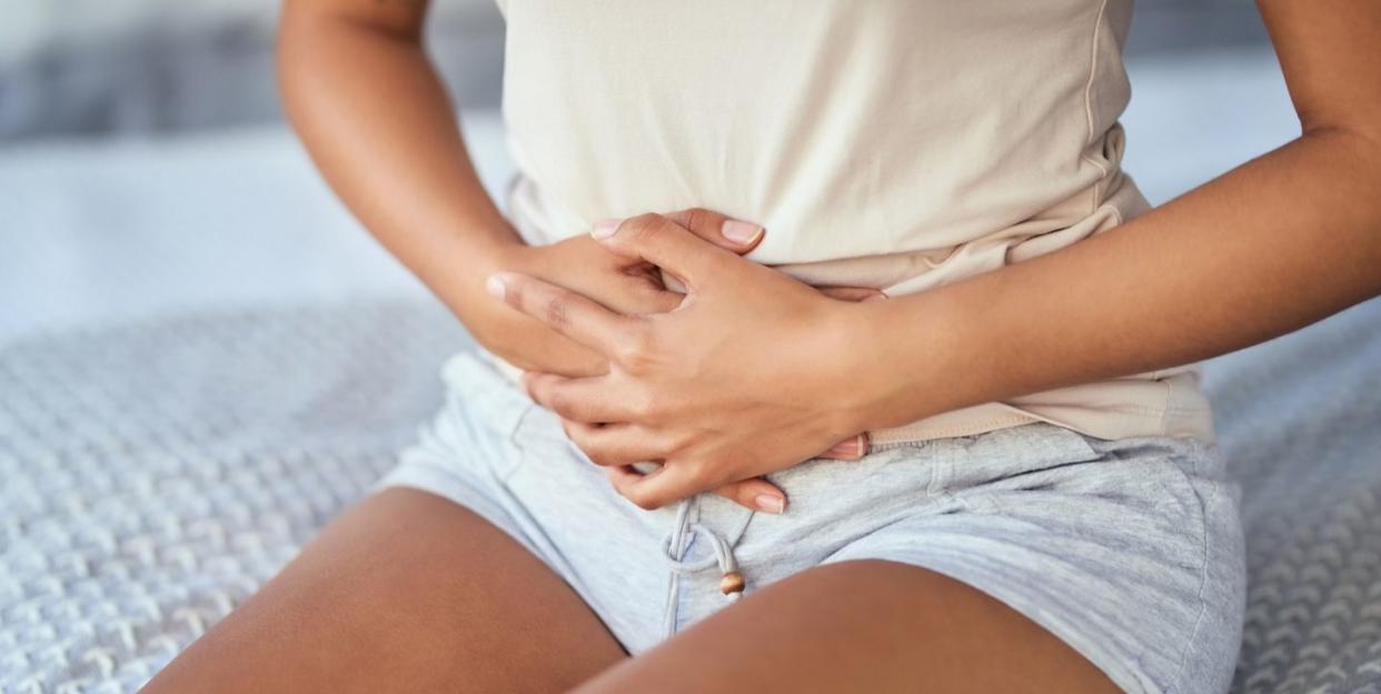 cropped shot of a young woman suffering from stomach cramps in her bedroom