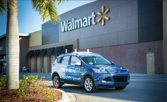 A blue car drives through the parking lot of a Walmart store.