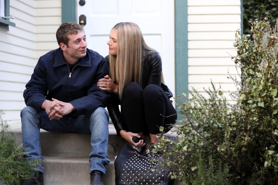 Two people sitting close on stairs, smiling and looking at each other with affection