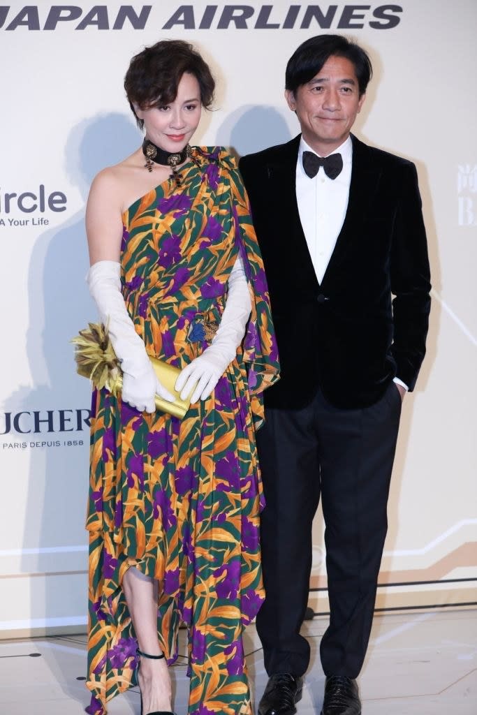 posing together, Tony wears a classic tux with a velvet jacket, and Carina wears a flowy one-shouldered floral dress with long opera gloves