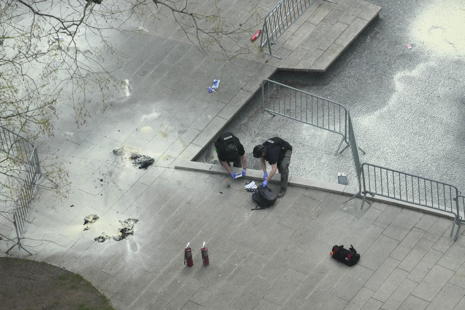 New York Police officers inspect a backpack left at the scene where a man lit himself on fire in a park outside Manhattan criminal court, Friday, April 19, 2024, in New York. Emergency crews rushed away a person on a stretcher after fire was extinguished outside the Manhattan courthouse where jury selection was taking place in former President Donald Trump's hush money criminal case. (AP Photo/Mary Altaffer)