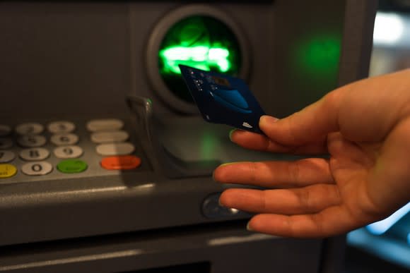 Close-up of woman inserting card into an ATM machine.