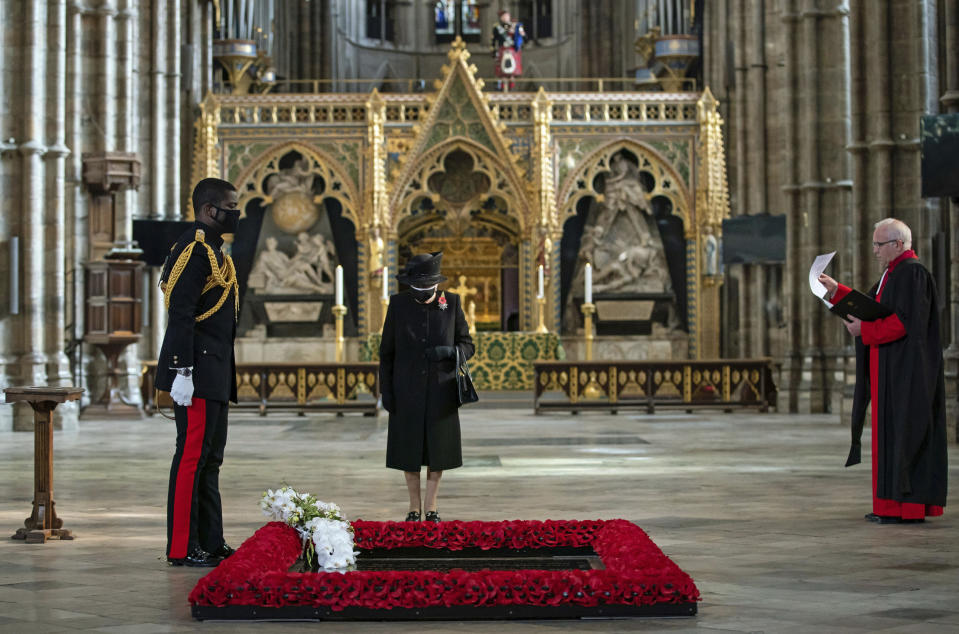 The Dean of Westminster Abbey David Hoyle, right, watches as The Queen's Equerry, Lieutenant Colonel Nana Kofi Twumasi-Ankrah, places a bouquet of flowers at the grave of the Unknown Warrior in front of Britain's Queen Elizabeth II, during a ceremony to mark the centenary of the burial of the Unknown Warrior, in Westminster Abbey, London, Wednesday, Nov. 4, 2020. Queen Elizabeth II donned a face mask in public for the first time during the coronavirus pandemic when attending a brief ceremony at Westminster Abbey last week to mark the centenary of the burial of the Unknown Warrior. While the 94-year-old has been seen in public on several occasions over the past few months, she has not worn a face covering. (Aaron Chown/Pool Photo via AP)