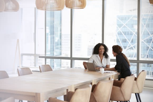 Two businesswomen using laptop in boardroom meeting.