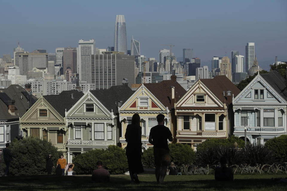FILE - In this Feb. 26, 2020, file photo, visitors look toward the "Painted Ladies," a row of historical Victorian homes, in front of the San Francisco skyline from Alamo Square Park in San Francisco. An estimate released Friday, May 1, 2020, by the California Department of Finance said that more people are leaving California than moving in, evidence of the toll the state's housing crisis is taking as the world's fifth largest economy inches toward 40 million people. (AP Photo/Jeff Chiu, File)