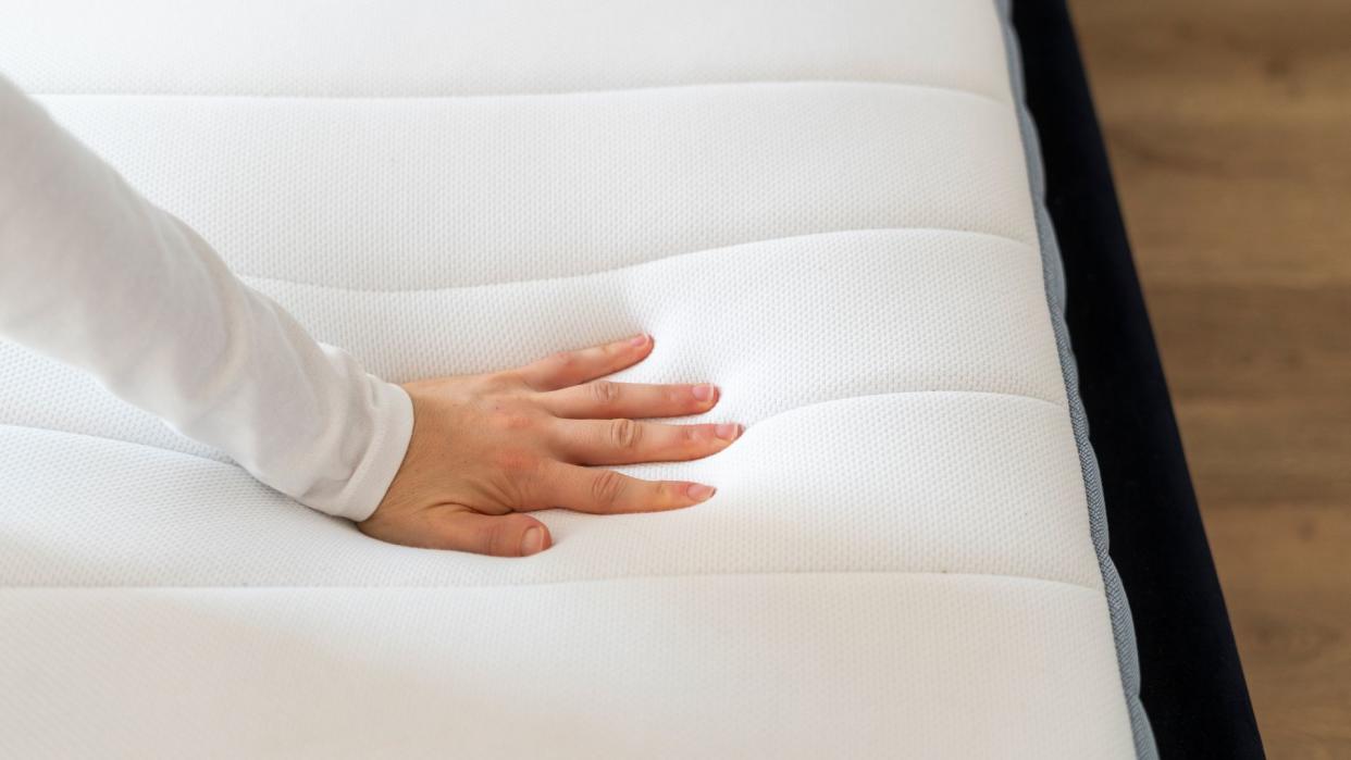  A woman's hand feels a memory foam mattress to check if it needs replacing. 