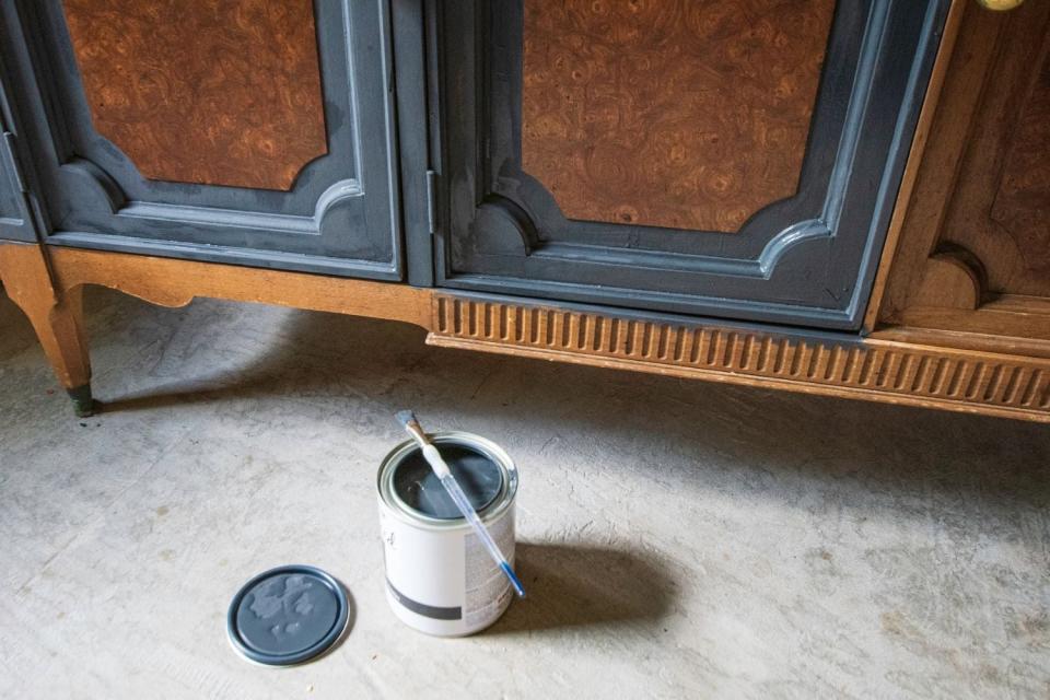 A can of paint sits open on the ground in front of a piece of furniture. 