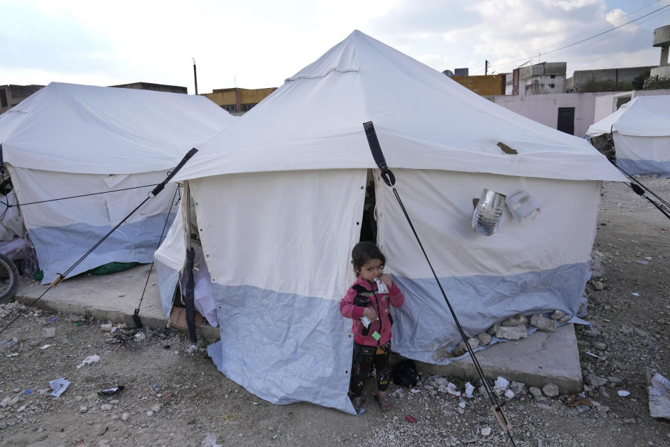 A girl whose family lost their home in the devastating earthquake stands outside a tent at a shelter camp in Killi, Syria, Sunday, Feb. 12, 2023. Destruction from the earthquake has killed tens of thousands and left millions more homeless in southern Turkey and northern Syria. (AP Photo/Hussein Malla)