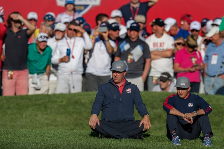 Team USA's Phil Mickelson (C) and Ricky Fowler sit on the grass as they watch their teammates play the afternoon four-balls matches during the 2016 Ryder Cup, at Hazeltine National Golf Course in Chaska, Minnesota, on September 30