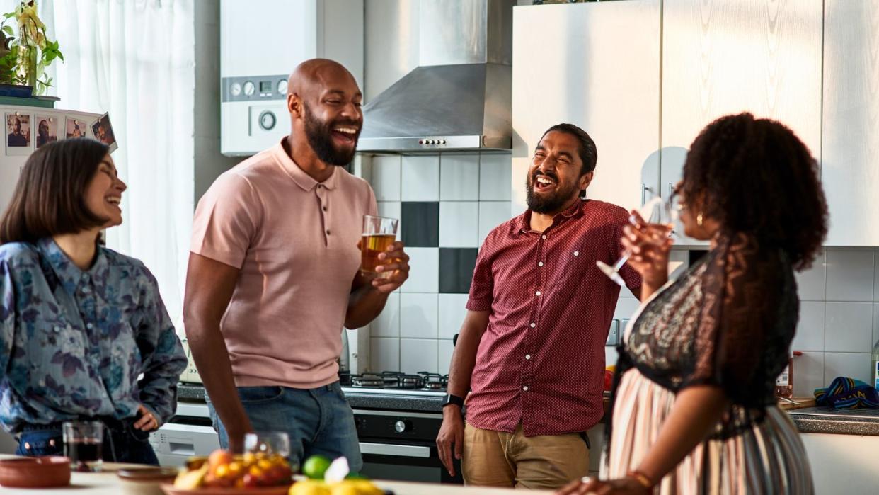 four people talking and smiling with drinks in kitchen