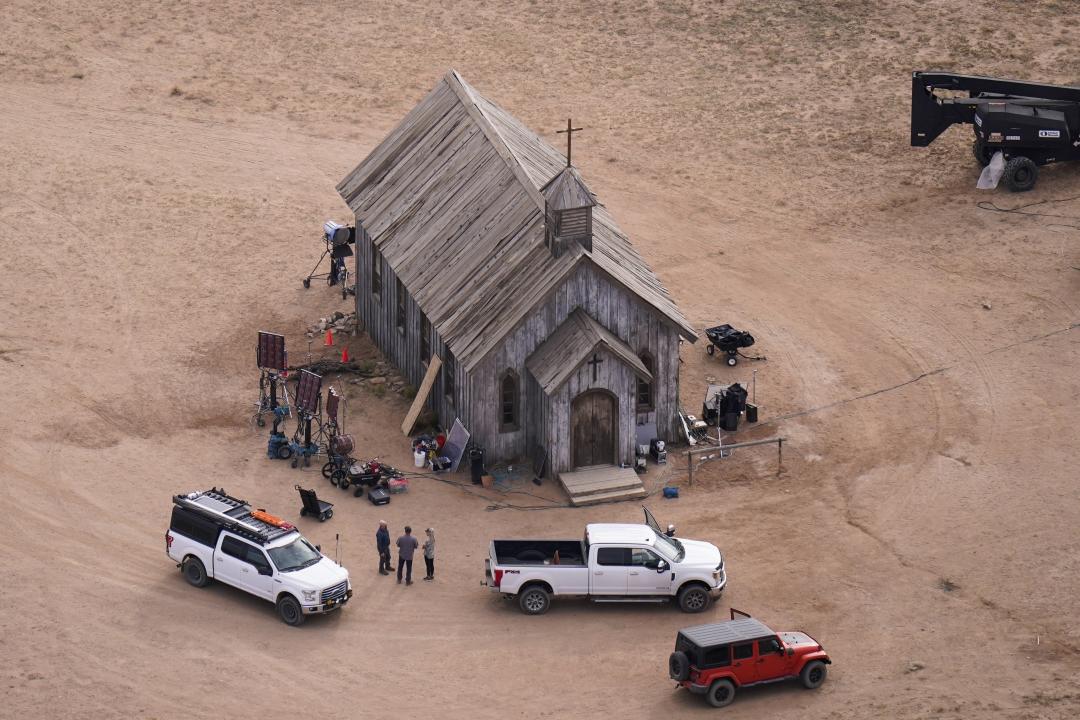 The movie set of Rust, with several vehicles parked around a wooden church.