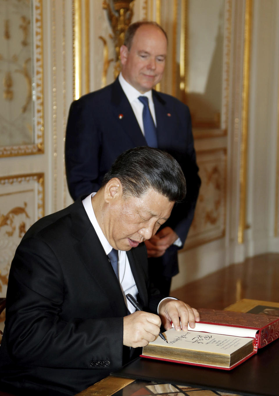 Chinese President Xi Jinping, foreground, signs the register of heads of state as Prince Albert II of Monaco looks on at Monaco Palace, Sunday, March 24, 2019. Xi is paying the first state visit by a Chinese president to the tiny Mediterranean principality of Monaco on Sunday. (Eric Gaillard/Pool Photo via AP)