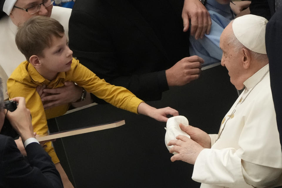 A child hands to Pope Francis a skullcap at the end of the weekly general audience at the Vatican, Wednesday, Dec.13, 2023. (AP Photo/Gregorio Borgia)