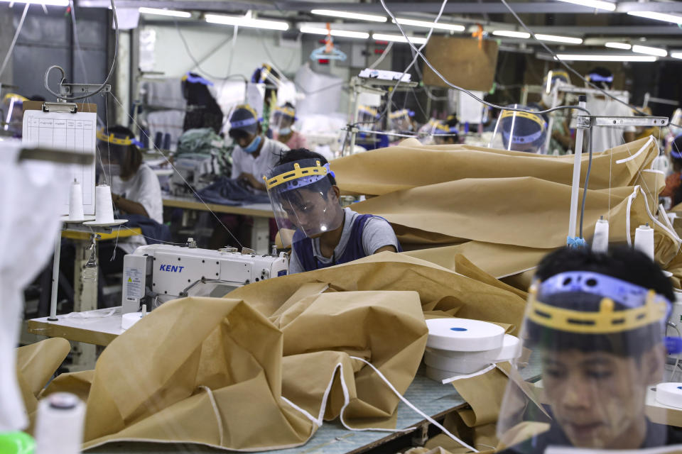 Workers wearing face mask and face shield to help curb the spread of the new coronavirus, sew surgical gown as they work at a garment factory Thursday, May 28, 2020, at Industrial Zone in Yangon, Myanmar. Despite a poor public health infrastructure and crowded urban areas, Myanmar has reported a surprising low number of COVID-19 cases, with just a little over 200 confirmed and a few deaths. (AP Photo/Thein Zaw)