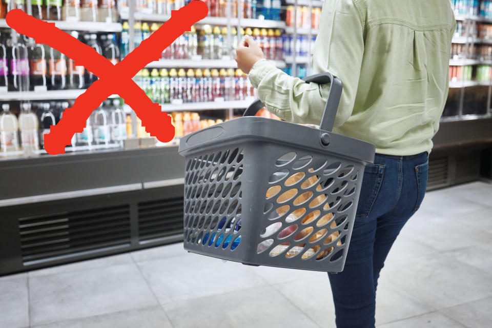 woman carrying a grocery basket past refrigerators stocked with bottled drinks