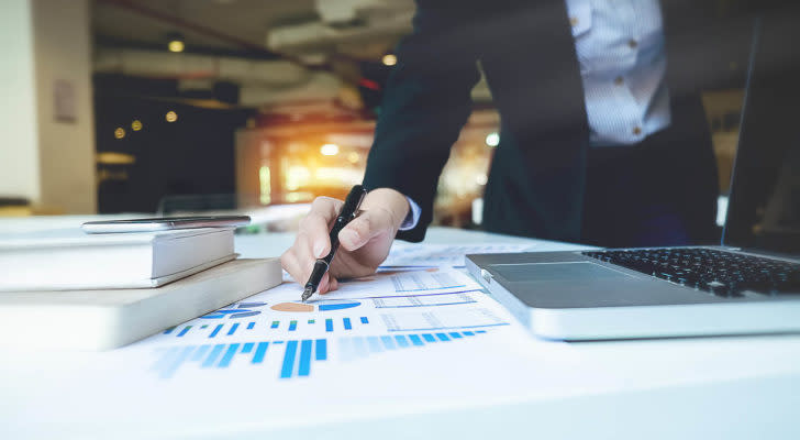 A photo of a businesswoman pointing at charts on a piece of paper on a table.