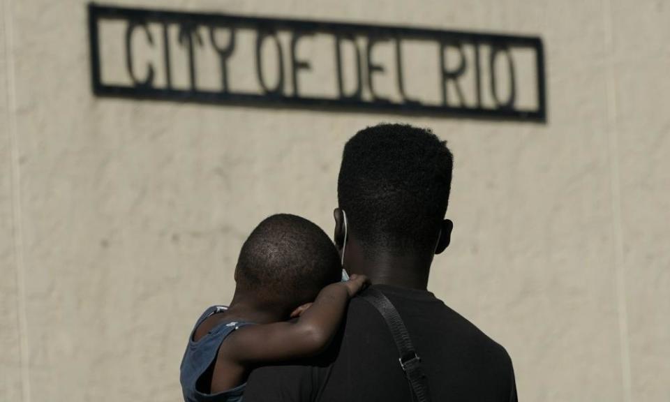 A Haitian man carries a boy while waiting to board a bus provided by a humanitarian group after being released from US custody in Del Rio, Texas.